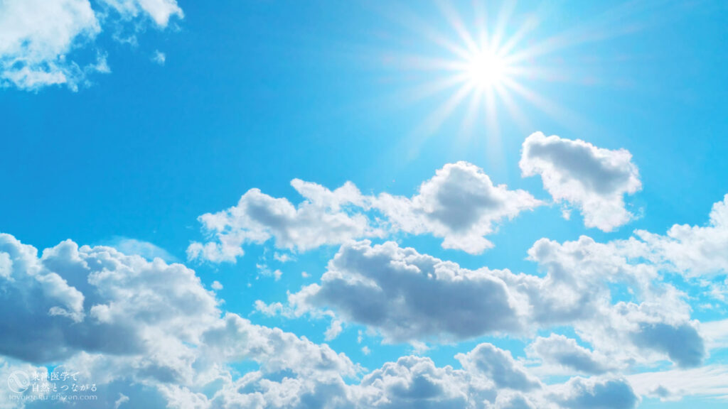 二十四節気「夏至」のイメージ。雲が浮かぶ青空に昇る太陽